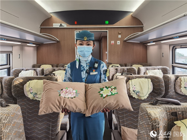 趙瑩靜展示中老鐵路國(guó)際旅客列車?yán)飵в兄袊?guó)牡丹花和老撾占巴花刺繡圖案的靠墊。人民網(wǎng)記者 杜明明攝